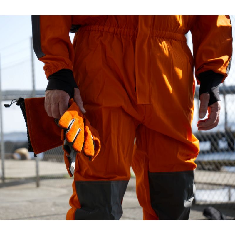 Operatör i blästringsdräkt håller HERO-handskar i handen – tydlig vy av handskenas baksida och förstärkningar.