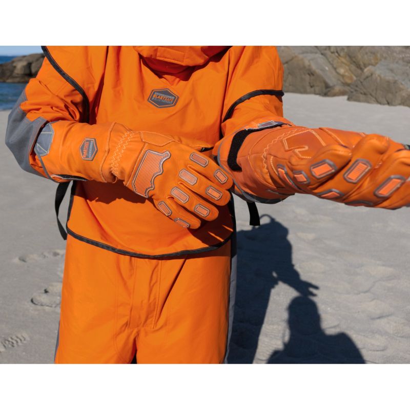 Blästringsoperatör i skyddsoverall som justerar IRONGRIP-handskar på stranden – visar skyddsutrustning i praktisk användning.