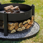 Närbild på MONTANA X eldfat med ved, stående på dekorativ stenplatta utomhus.