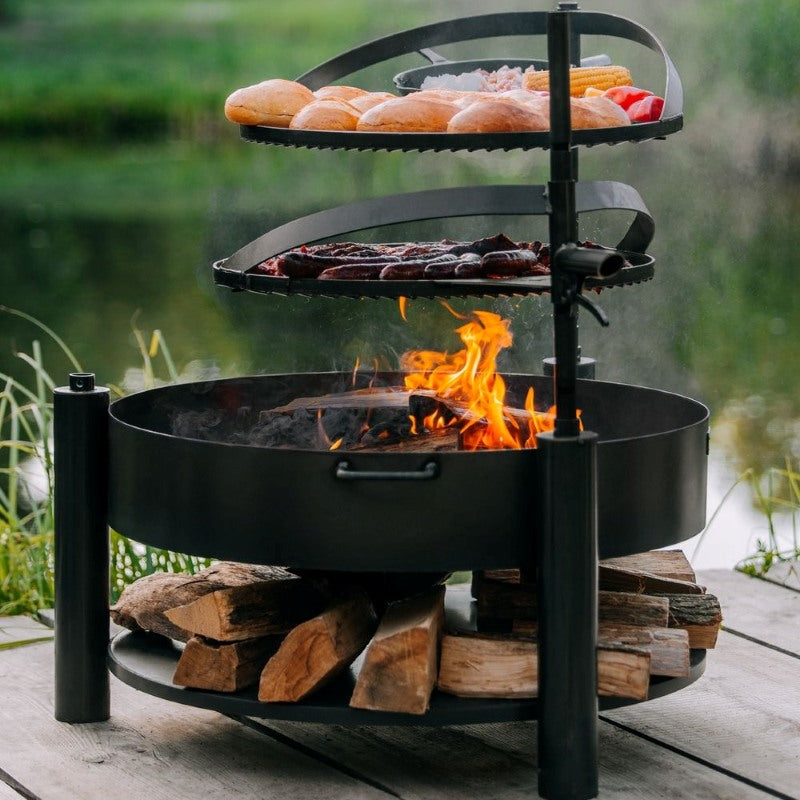 Eldfat MONTANA X med levande eld, två grillnivåer och mat som tillagas över elden.