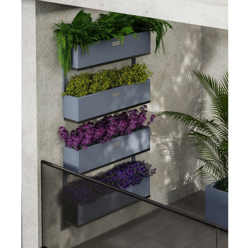 Fyra väggmonterade Coyotto planteringskärl i stål, fyllda med färgstarka växter och placerade på en balkongvägg med grönskande omgivning.