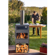 Kamin och vedställ utomhus på trädäck med trädgård i bakgrunden.