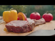 Uppskärning av grillat kött bredvid MONTANA X eldfat med dubbla grillgaller över öppen eld.