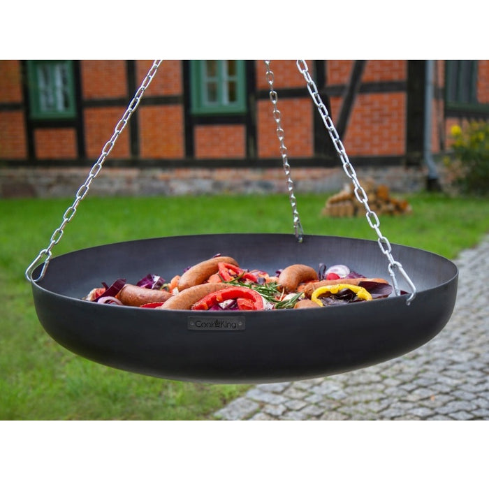 Wok från Cook King med grillad mat, upphängd på stativ framför husvägg.